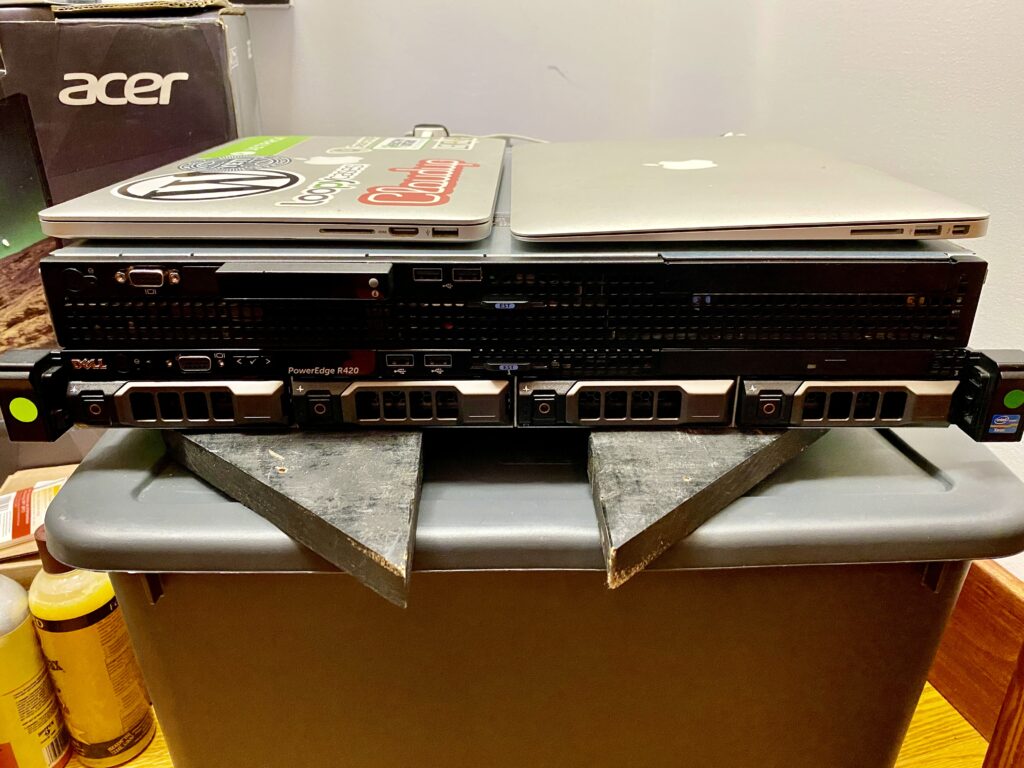 A Dell Poweredge R210 II, Dell Poweredge R420, and Apple MacBooks stacked on top of each other